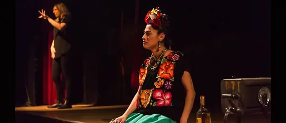 Cena com atriz de figurino Frida Kahlo ao fundo intérprete de Libras